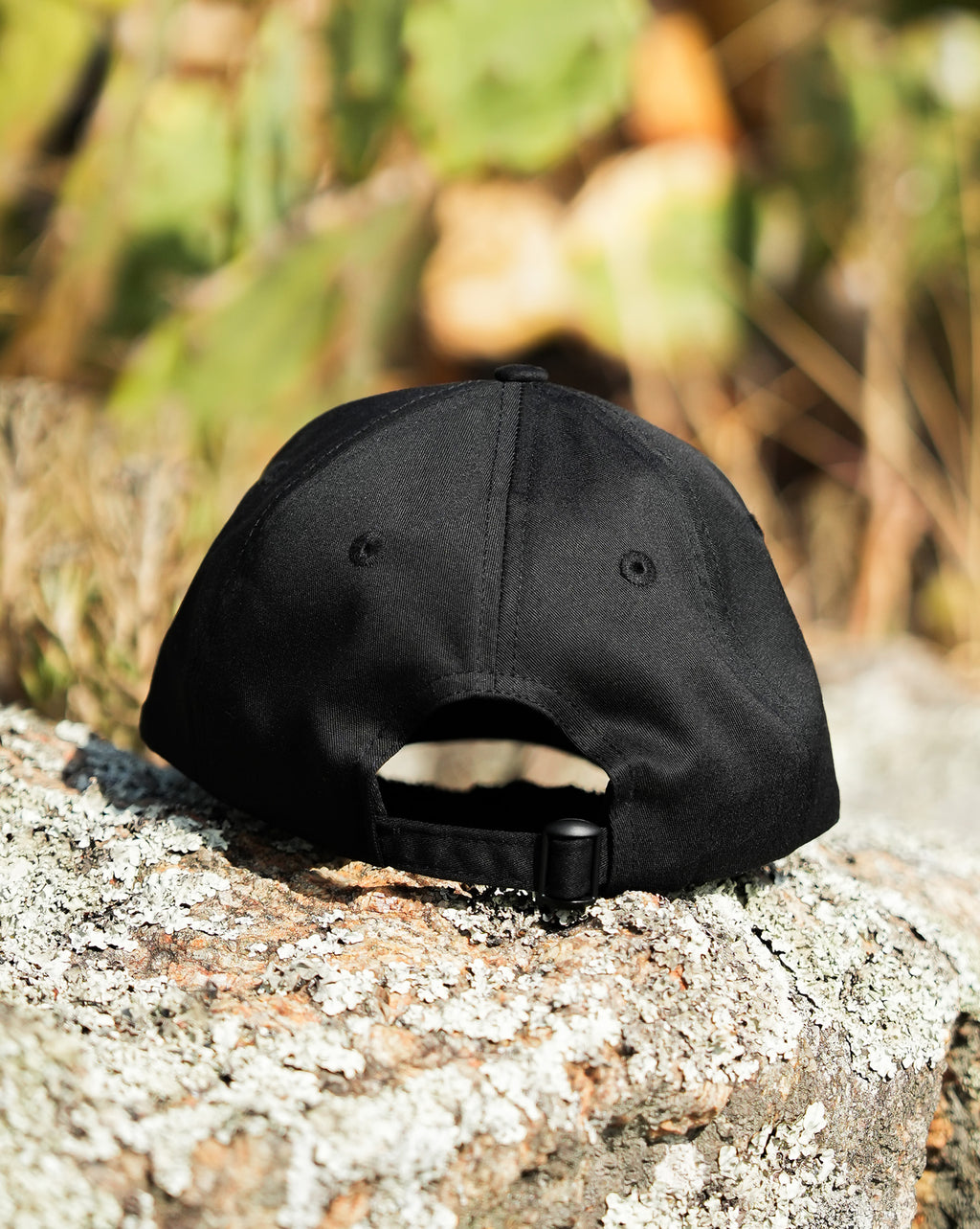 Foto em ambiente natural mostrando a parte de trás do boné Volcom preto, com textura de fundo em tronco de árvore.