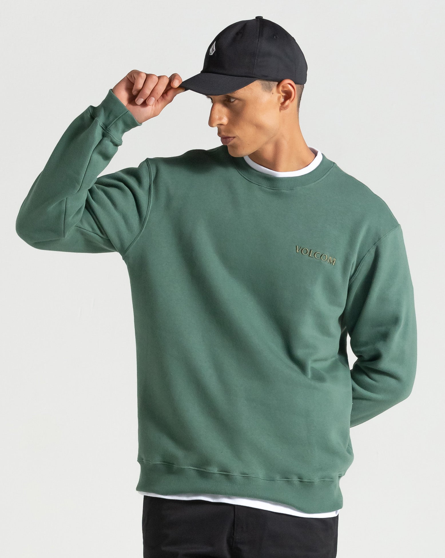 Modelo vestindo boné preto Volcom com moletom verde, imagem de lifestyle para destacar estilo urbano e casual.