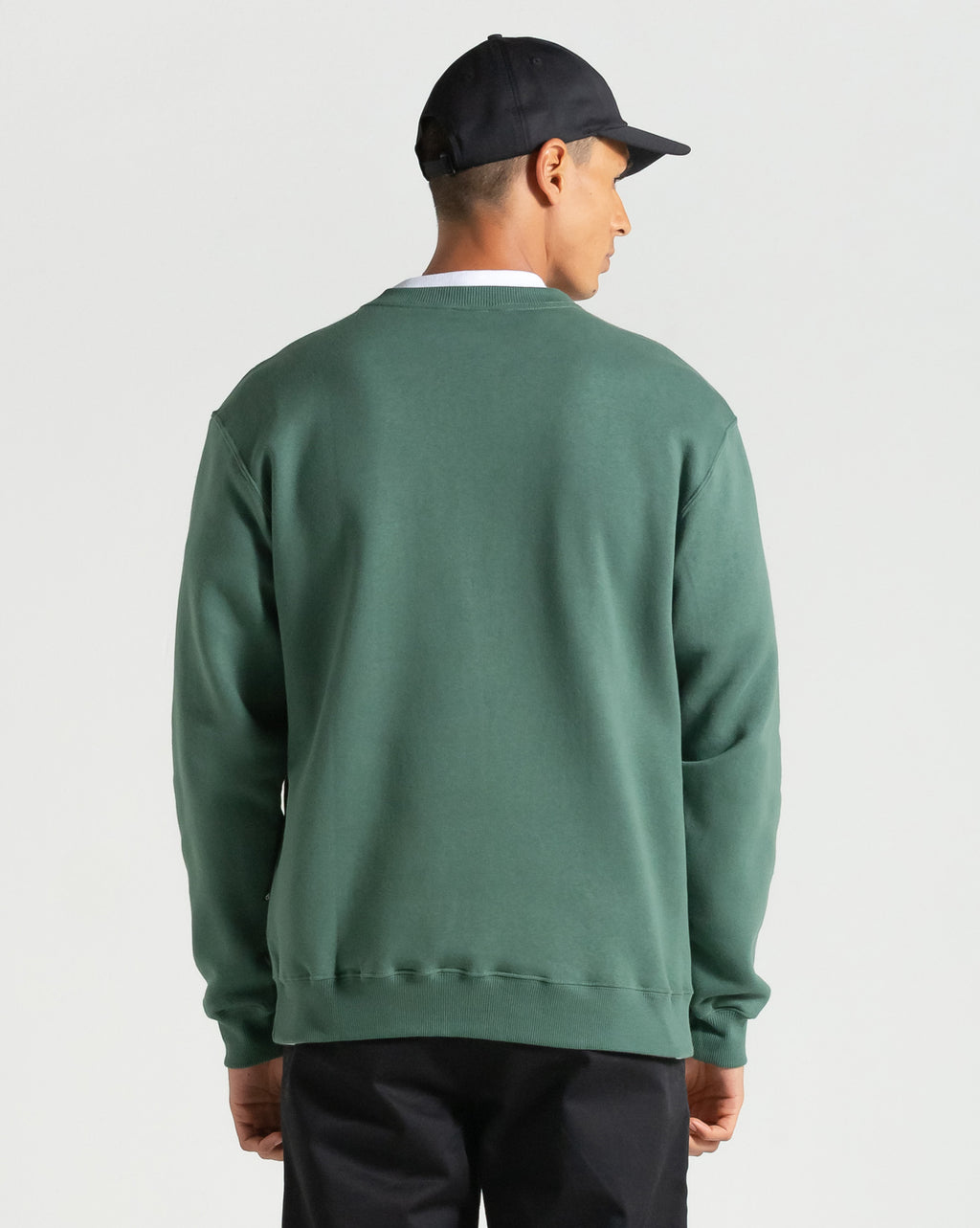 Imagem do boné Volcom preto sendo usado por modelo, vista traseira em look completo com moletom verde, ideal para mostrar caimento.