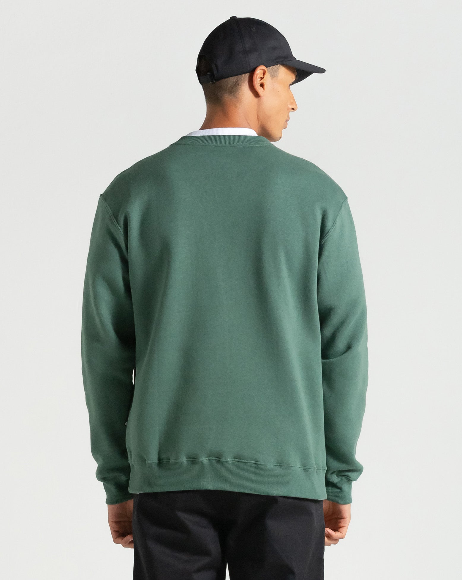 Imagem do boné Volcom preto sendo usado por modelo, vista traseira em look completo com moletom verde, ideal para mostrar caimento.