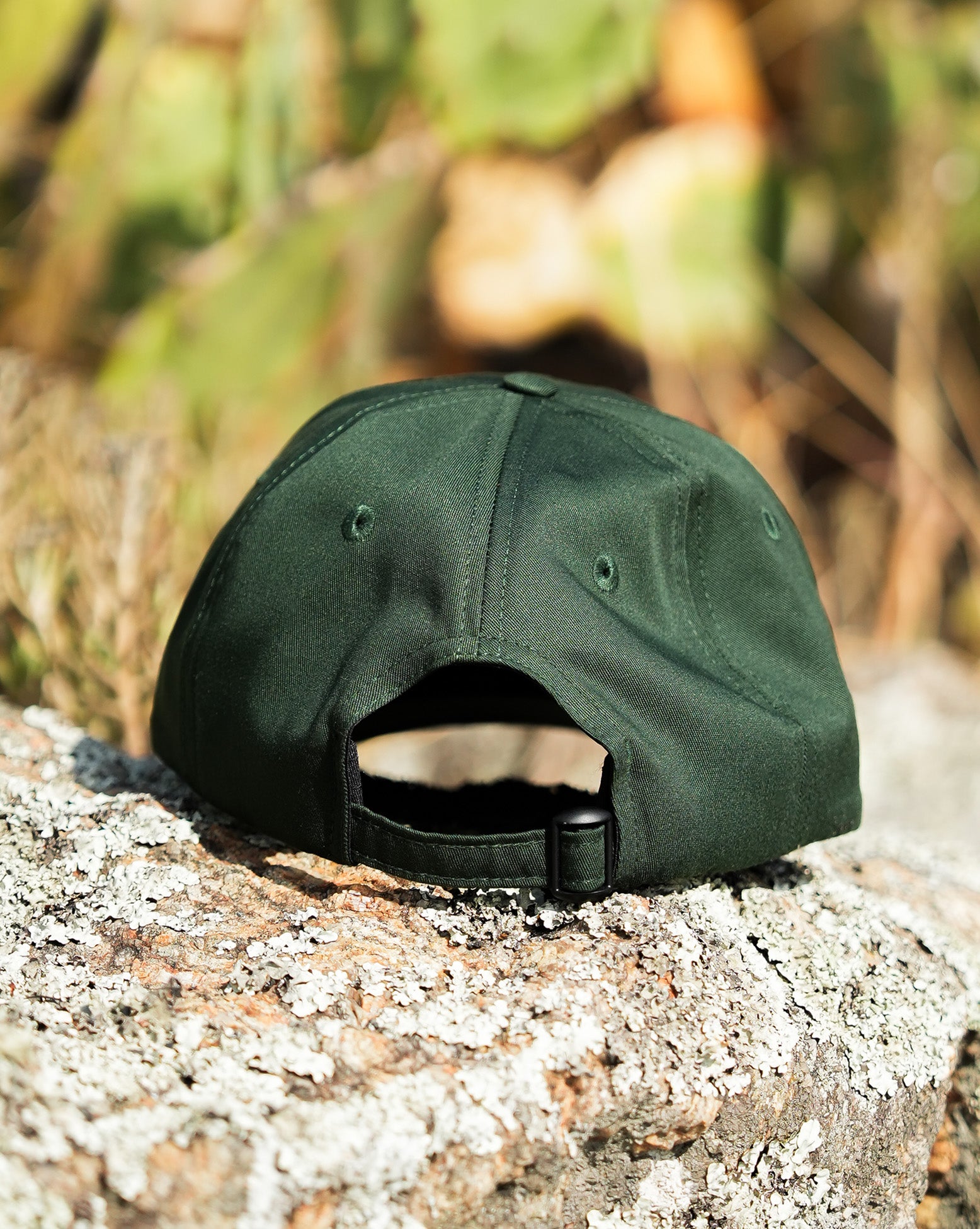 Mostra a parte traseira do boné Volcom verde com fecho ajustável, fotografado em ambiente natural com textura de tronco e fundo desfocado.