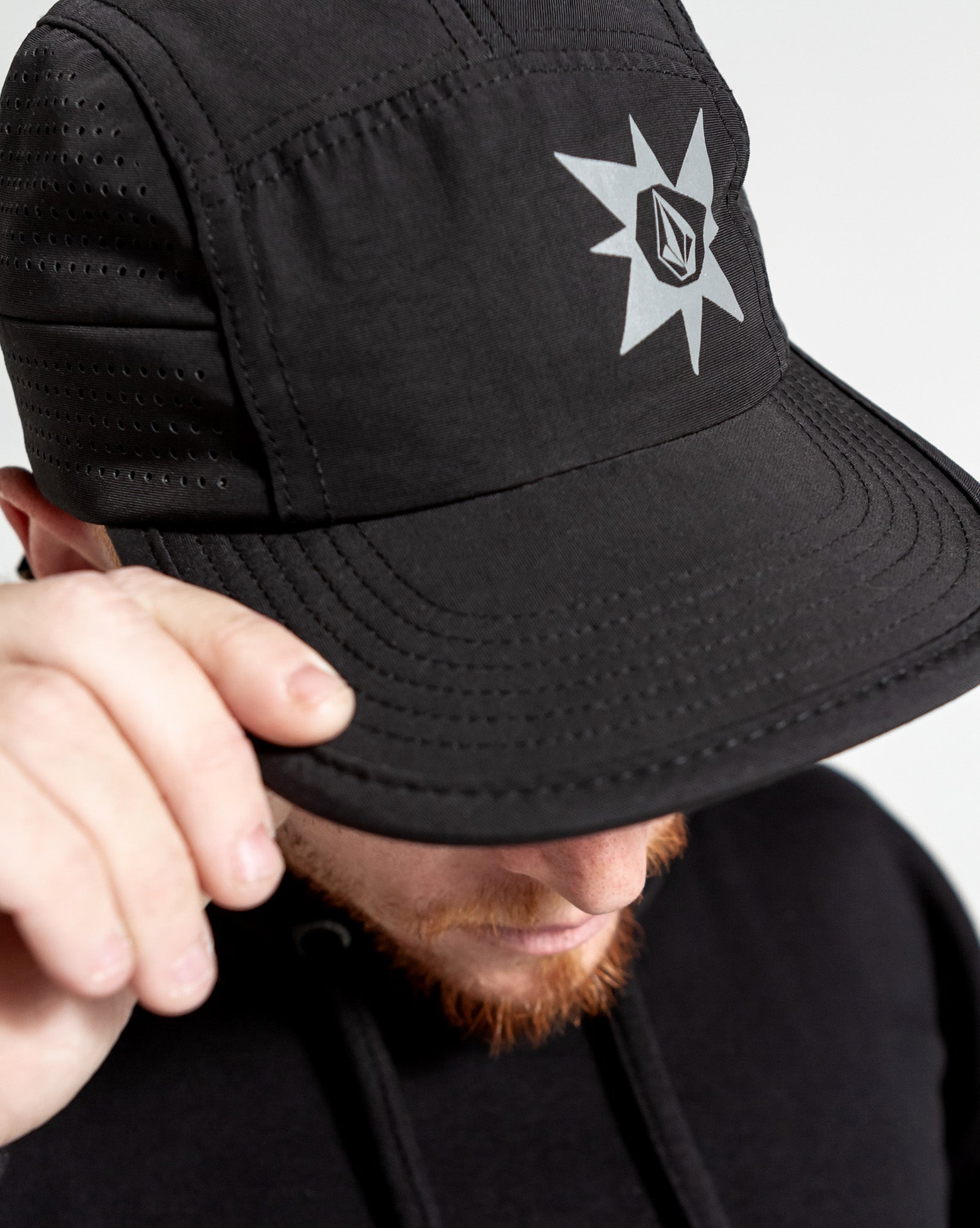 Bone Volcom TT Sense na cor preta, com logo em destaque, sendo ajustada por uma mão.