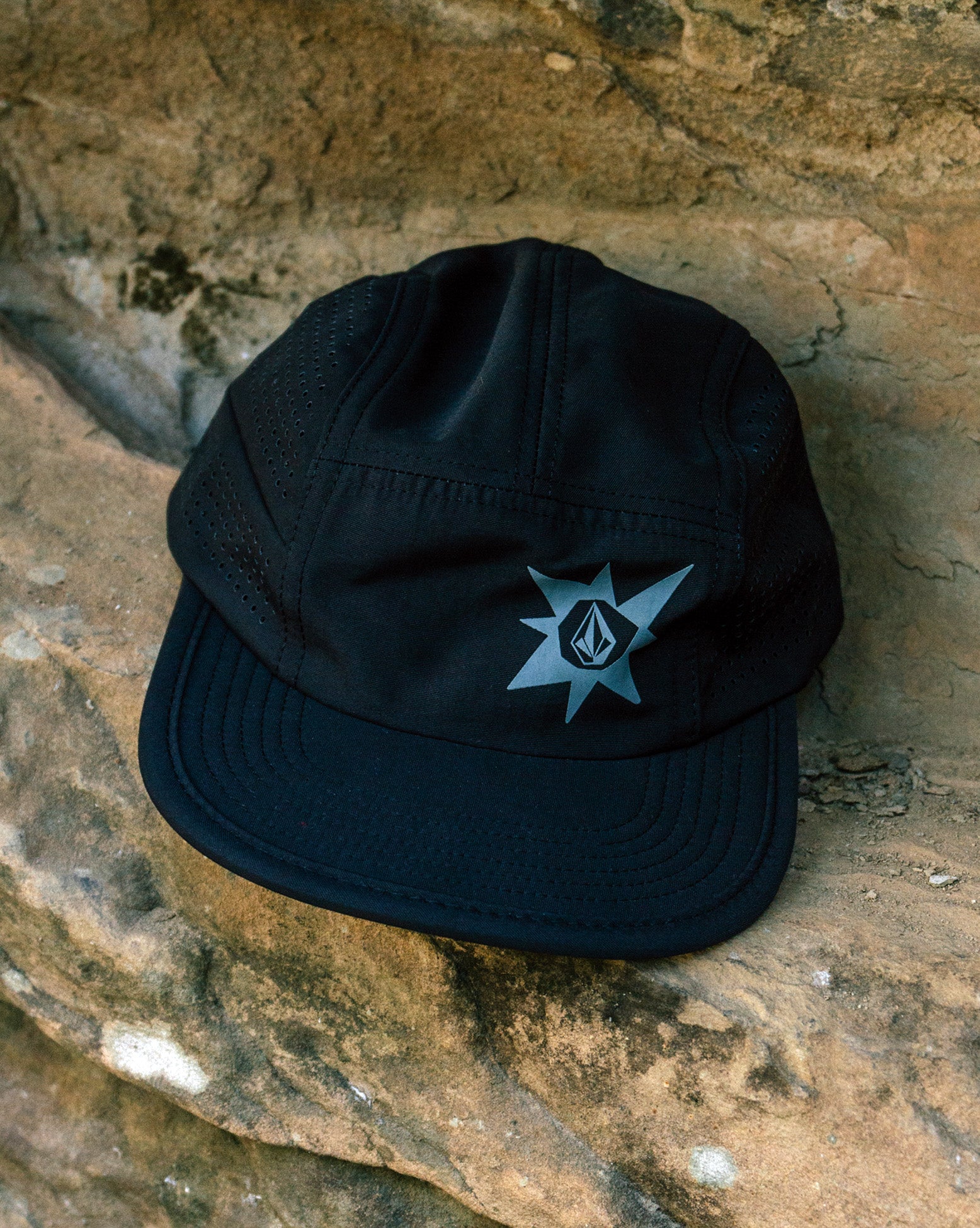 Boné preto Volcom TT Sense com logo frontal em tom cinza, colocado sobre pedra de textura rústica