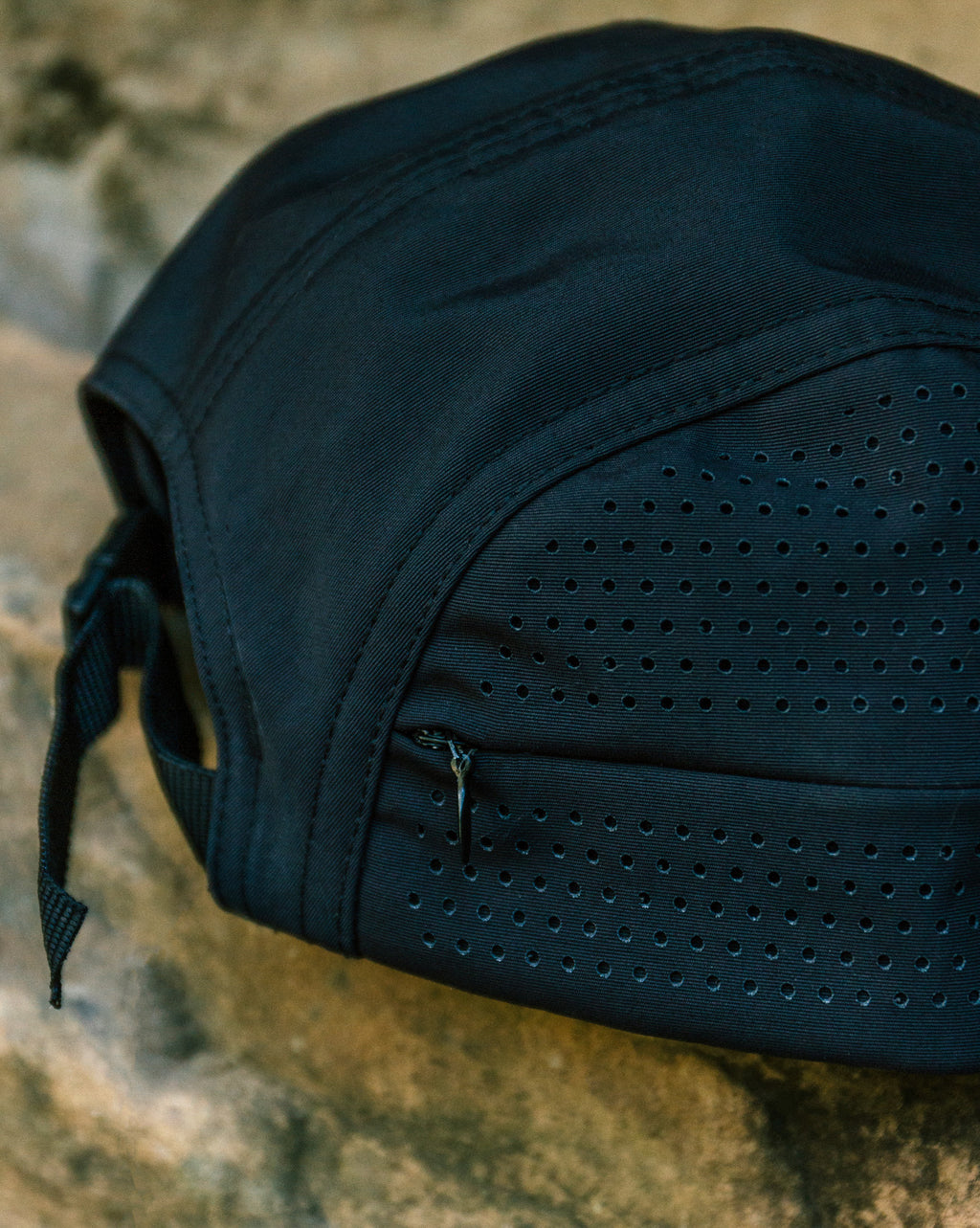 Bone preto Volcom TT Sense com detalhe de pequenos furos e zíper, apoiado sobre superfície de pedra