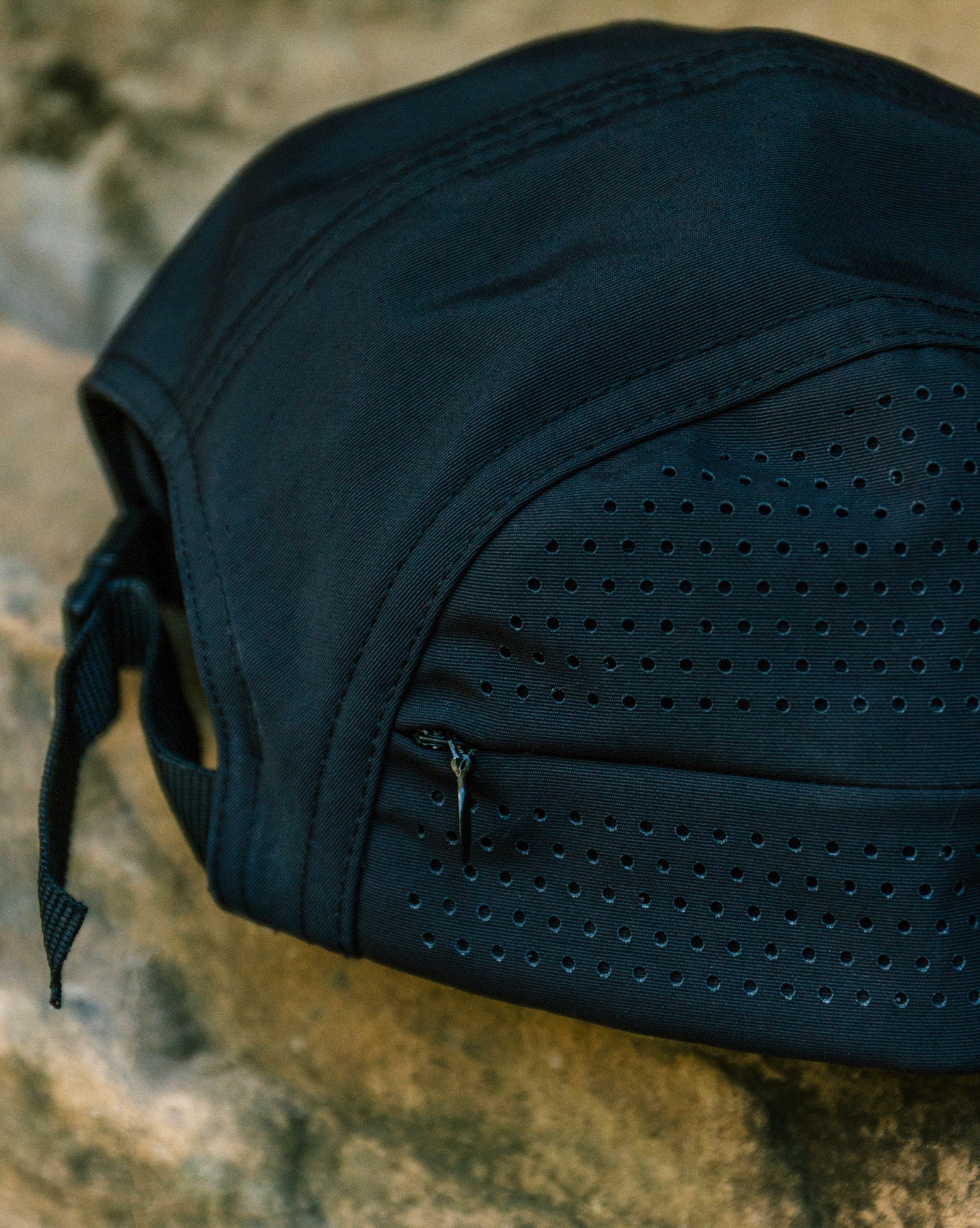 Bone preto Volcom TT Sense com detalhe de pequenos furos e zíper, apoiado sobre superfície de pedra